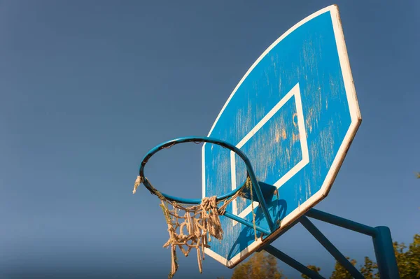 Velho arco de basquete rasgado contra um fundo azul céu. — Fotografia de Stock