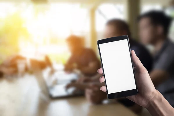 Closeup of Hand holding Blank Screen of Smart phone with business group of teamwork anywhere working together in office blur background. Smart phone with blank screen and can be add your texts or others on smart phone.