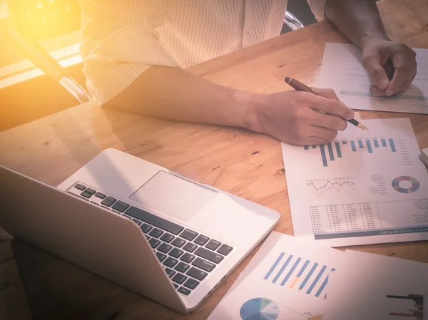 iş adamı el dizüstü bilgisayarda iş grafik bilgi diyagramı ahşap masa üzerinde çalışmak için kalem tutan kapatın. Vintage etkisi.