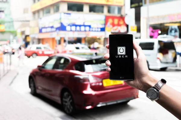 香港、中国 - 2016年5月16日 :道路や赤い車でLg G4に表示されるUberアプリを持つ男の手、Uberはスマートフォンアプリベースの交通ネットワークです. — ストック写真