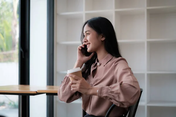 Bir kafede, genç ve güzel bir kadın telefonda bir fincan kahveyle konuşuyor. müşterisi için randevu ayarlamak ve sohbet etmek. — Stok fotoğraf