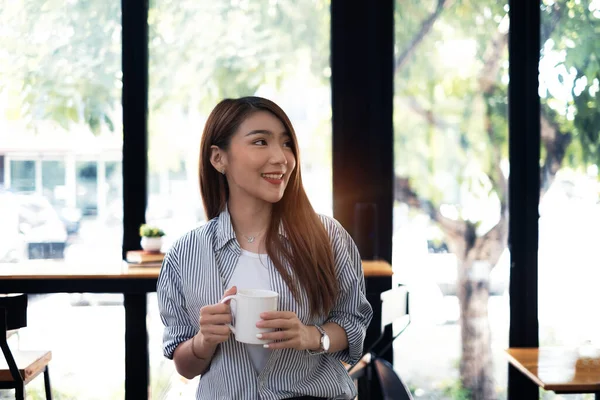 Ung vacker kvinna som håller kaffekopp och känner sig fräsch när hon sitter på sin arbetsplats på måndag morgon. — Stockfoto