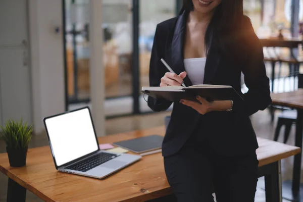 Happy business woman taking note with laptop on wooden desk in office — Foto de Stock