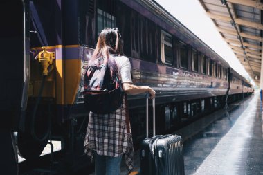 Bir tren istasyonunda sırt çantasıyla trene binmeyi bekleyen bir kadının görüntüsü. tek başına seyahat kavramı