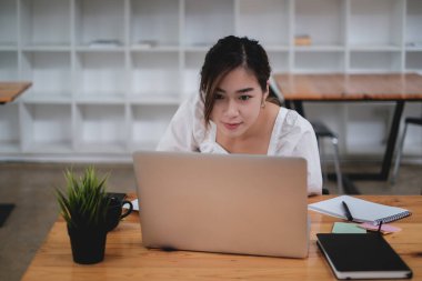 Asyalı İş kadını video görüşmesine odaklanıyor ve ofiste dizüstü bilgisayarla ahşap masada oturuyor..