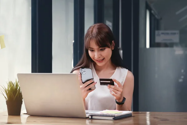 Жінка насолоджується онлайн-додатком для покупок і дивиться на кредитну картку для заповнення номера до оплати — стокове фото