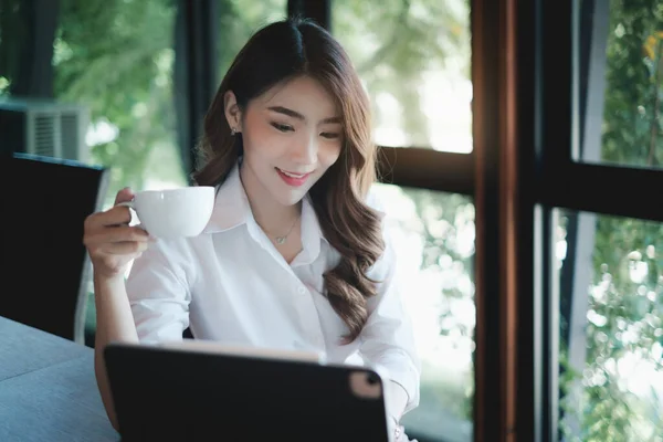 Güzel bir iş kadınının elinde bir fincan kahve tutup işe gitmeden önce e-postalarını kontrol etmesi. — Stok fotoğraf