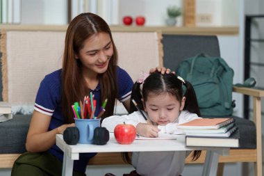 Bir anne, kızına ev ödevlerinde yardım eder, rahat oturma odasında destekleyici bir öğrenme ortamı sağlar..