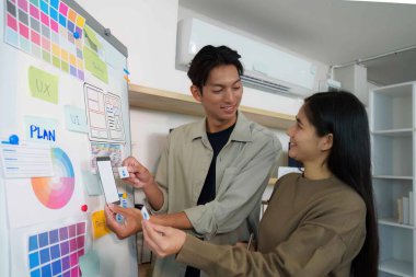 Genç bir adam ve kadın, renkli planlama malzemeleriyle çevrili UI tasarımı hakkında yaratıcı bir tartışmaya girişiyor..