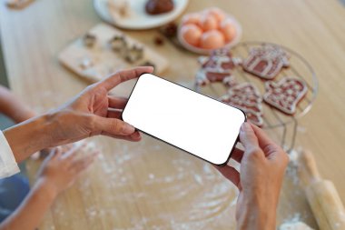 Bir insan kurabiye pişirme anını yakalar. İçi malzemelerle dolu sıcak bir mutfakta akıllı telefon tutar..