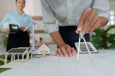 An architect utilizes a compass on design plans, surrounded by sustainable models, showcasing eco-friendly architecture.