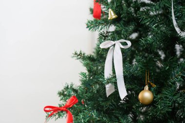 A close-up of a Christmas tree adorned with a white ribbon and golden ornament, showcasing holiday elegance and charm.