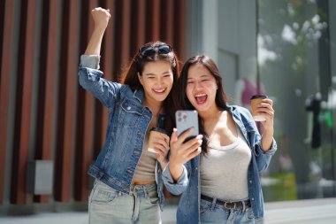 İki arkadaş neşeyle bir anı kutluyorlar, kahve fincanları tutuyorlar ve şehir ortamında kahkahaları atıyorlar..