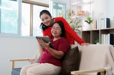 Bir anne ve kızı, tablet kullanırken neşeli bir anı paylaşıyor, yakın ilişkilerini parlak bir ev ortamında gösteriyorlar..