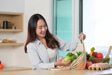 Genç bir kadın neşeyle taze meyve ve sebze seçiyor, sürdürülebilirliği teşvik ediyor ve modern mutfağında sağlıklı bir yaşam sürüyor..