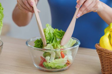 Bir kadın taze salata malzemelerini ahşap çatallarla karıştırıyor, sağlıklı beslenmeyi ve sağlıklı beslenmeyi parlak bir mutfakta teşvik ediyor..