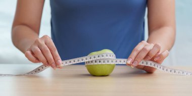 Yeşil bir elmayı mezurayla ölçen biri, sağlıklı beslenme ve sağlıklı beslenme alışkanlıklarını vurguluyor..