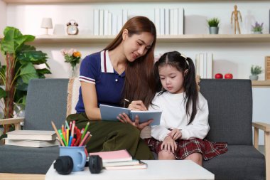 Şefkatli bir anne, kızına rahat bir oturma odasında derslerinde yardımcı olur. Öğrenme ve kaynaşmayı teşvik eder..