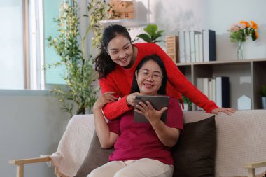 Bir kız ve anne, sıcak bir ev ortamında gülücüklerini ve gülüşlerini paylaşan bir tabletle meşgul olurlar..