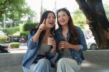 İki arkadaş ellerinde kahve fincanlarıyla keyifli bir anı paylaşıyor, açık havada gülüp sohbet ediyorlar..