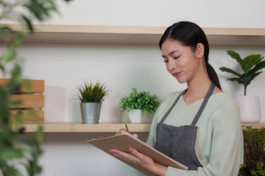 Rahat bir ortamda notlar yazarken gülümseyen genç bir kadın, çalışma alanındaki olumlu ve yaratıcılığı vurguluyor..