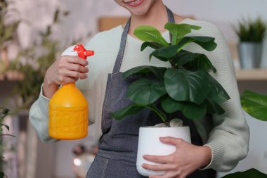 Bir kadın elinde sprey şişeyle elinde çiçeklerini buğulamaya hazır bir şekilde gülümsüyor..