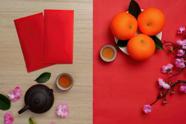 Renkli bir arkaplanda kırmızı zarflar, portakallar ve çay bulunan canlı bir Çin Yeni Yıl düzeneği..