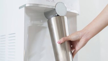 Bir el, su dağıtıcısının yanındaki paslanmaz çelik şişeye uzanıyor ve sürdürülebilir su tüketimi uygulamalarını vurguluyor..