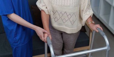 Bir bakıcı yaşlı bir kadın için yürüteci tutar, hareket eğitimi sırasında onun güvenliğini ve rahatlığını sağlar..