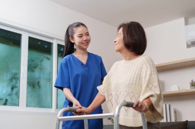 Bakıcı, yaşlı bir kadının yürüteç kullanmasına yardım eder. Hareket yardımını ve şefkatli bakımı vurgular..