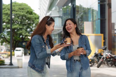 İki arkadaş, kahve yudumlarken ve modern bir binanın dışında sohbet ederken keyifli bir anı paylaşıyor, dostluk ve bağ sergiliyorlar..