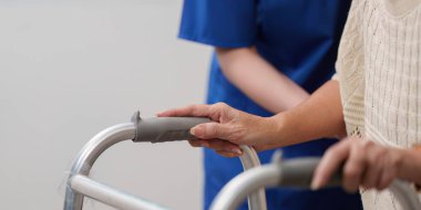 Şefkatli bir hemşire yaşlı bir kadına bir yürüteçle yol göstermesi için yardım eder. Ev ortamında bakım ve desteği vurgular..