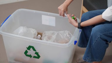 Bir kadın plastik şişeleri geri dönüşüm kutusuna yerleştiriyor, çevresel sürdürülebilirliğe ve sorumlu atık yönetimine katkıda bulunuyor.