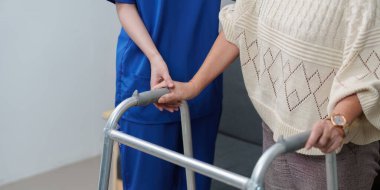 Bakıcı, yaşlı bir insanın elini nazikçe tutar. Yürüteç kullanır, sağlık hizmetlerindeki desteği ve merhameti sembolize eder..