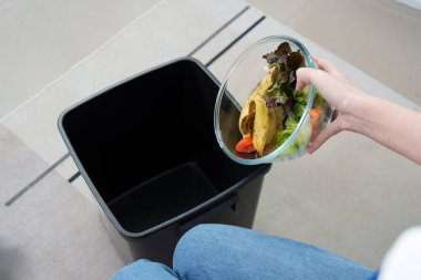 Atık yönetimi ve sürdürülebilirliğin önemini vurgulayarak, sebze artıklarını çöp kutusuna atan bir kişi.