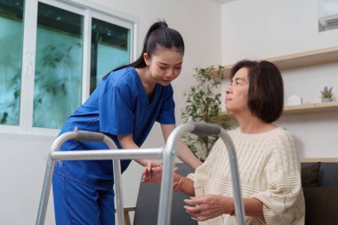 Kendini adamış bir hemşire, yaşlı bir kadına, bir ev ortamında yürüteç kullanarak, bakım ve destek göstererek yardım eder..