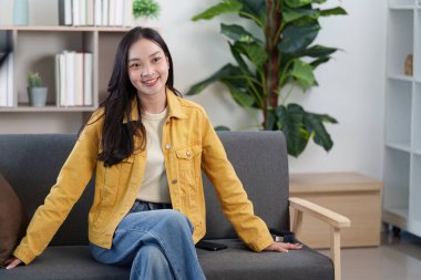 Neşeli bir kadın koltukta poz veriyor, hayat dolu kişiliğini ve rahat yaşam tarzını modern bir yaşam alanında sergiliyor..