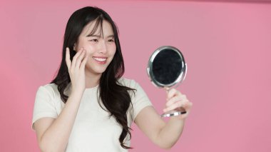 Neşeli kadın aynada tenini kontrol ediyor. Neşeli pembe bir çevrede güzelliği ve kendine bakımı kutluyor..