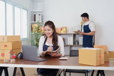 Masasındaki lojistik işleri verimli bir şekilde yöneten genç bir kadın, paketlerle çevrili, modern bir ofiste verimliliği vurguluyor..