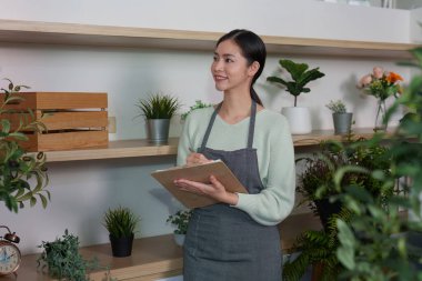 Neşeli bir kadın, modern kapalı bir bahçedeki bitkileri incelerken, bitki bakımı ve bahçıvanlığın neşesini ön plana çıkarıyor..