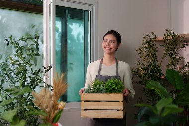 Gülümseyen bir kadın saksı bitkileriyle dolu ahşap bir sandık taşır, bahçe işleri ve bitki bakımının neşesini somutlaştırır..