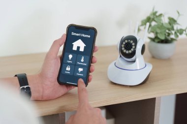 Genç bir adam akıllı ev aletlerini yönetmek için akıllı telefonunu kullanıyor. Ev otomasyonunda modern teknolojinin kolaylığını gösteriyor..