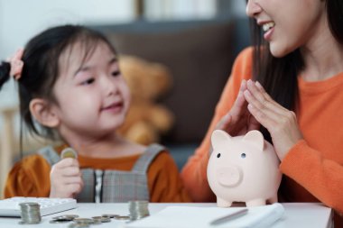 Bir çocuk ve ebeveyn, kumbarada para biriktirirken keyifli bir anı paylaşıyor, finansal okur yazarlığı destekliyor..