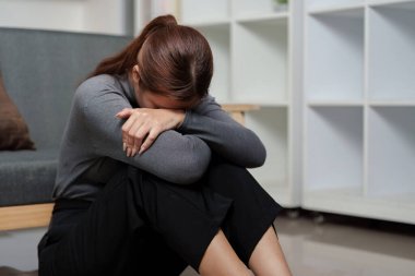 Kollarını dizlerine dolamış bir kadın zihinsel sağlık yolculuğunu ve kişisel bakım ihtiyacını yansıtıyor..