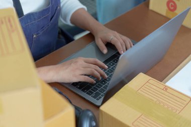 Küçük bir işletme sahibi, kargo kutularıyla çevrili bir dizüstü bilgisayarda girişimci ruhunu ve uzak çalışma yaşam tarzını sergiliyor..