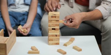 Bir baba oğluna Jenga oyununda rehberlik eder, rahat bir oturma odasında takım çalışmasını ve kahkahaları teşvik eder..