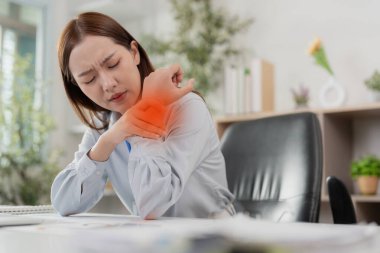 Genç bir kadın, masasında çalışırken dirseğini tutarak acı içinde kıvranıyor ve ofis sendromunun günlük hayattaki etkilerini anlatıyor..