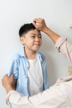 Bir baba sevgiyle oğlunun boyunu ölçer, bakım ve büyümeyi sembolize eder..