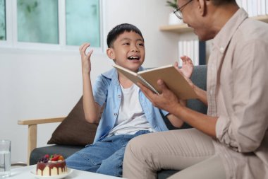 Bir baba ve oğul, sıcak bir oturma odasında neşeli bir kitap okuma seansına katılır..