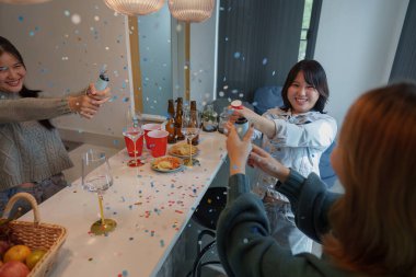 Arkadaşların içki ve konfeti püskürttüğü neşeli ve şen bir ortam yaratan canlı bir parti sahnesi..